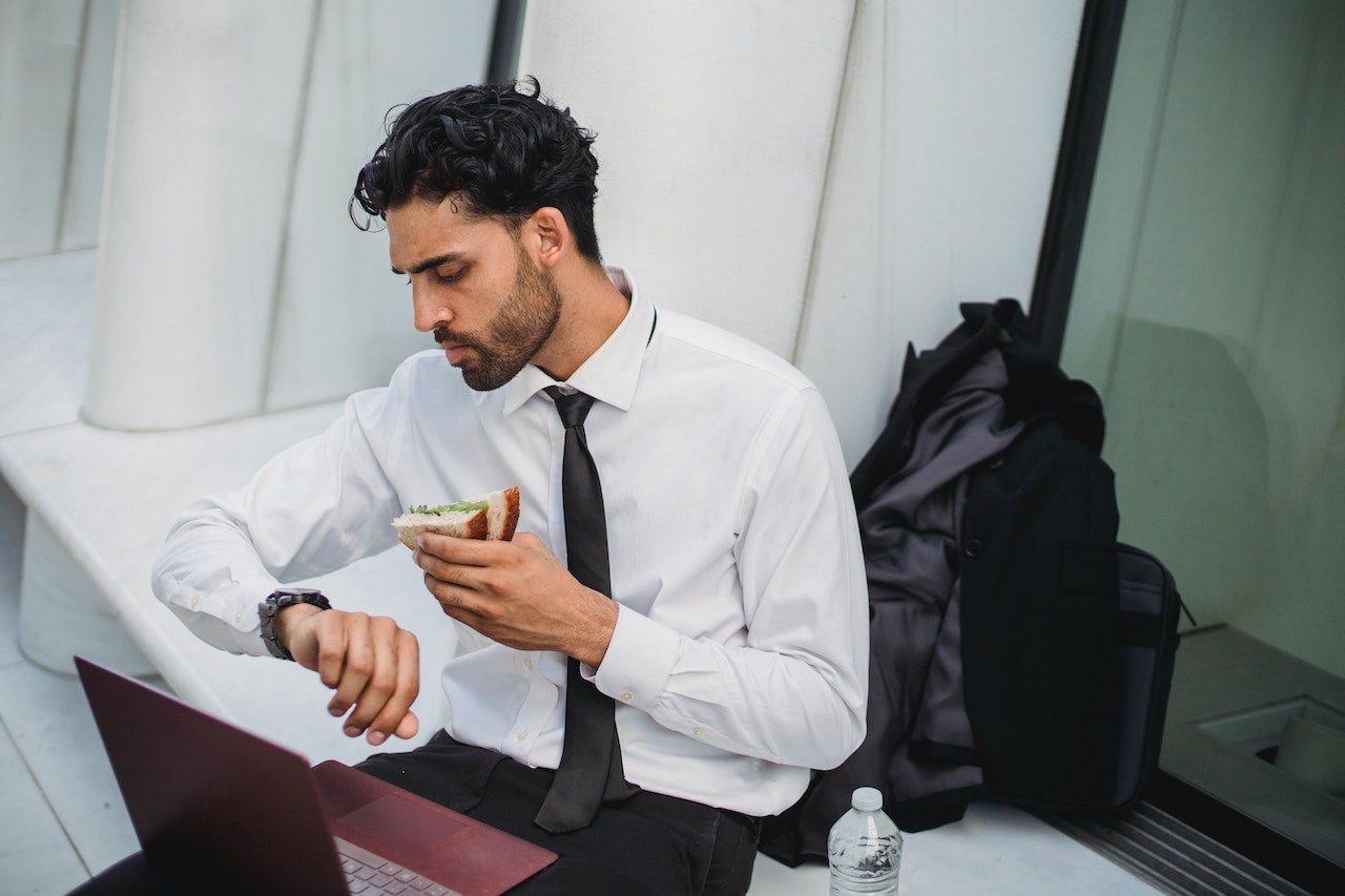Bearded-Man-in-a-suit-Looking-at-His-Watch-while-eating-a-Sandwich-eat-the-frog-meaning